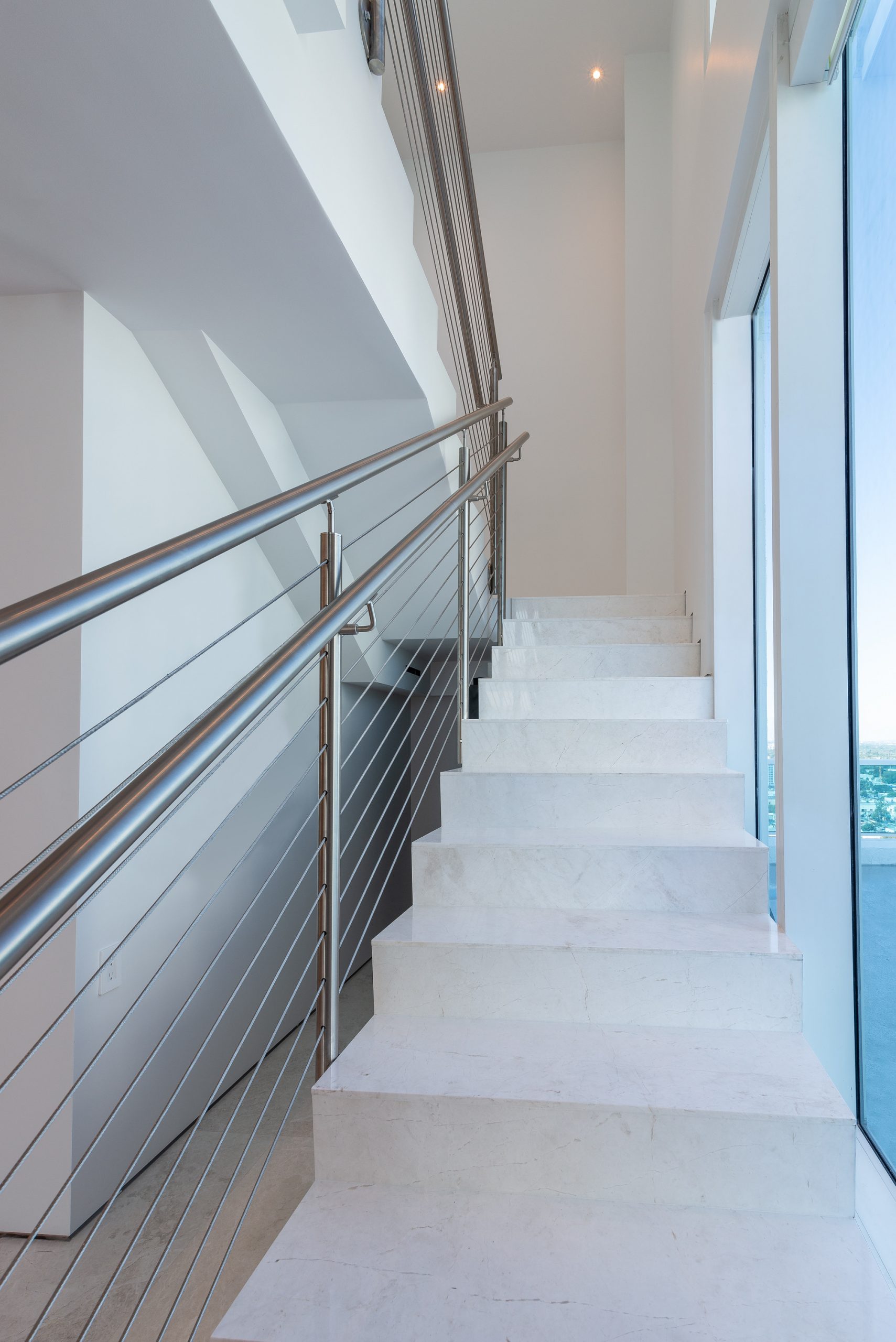 White stone staircase with stainless cable railing in a modern Miami residence