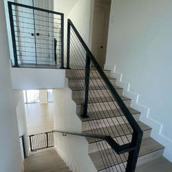 Modern black aluminum and cable railing beside floating wood stairs